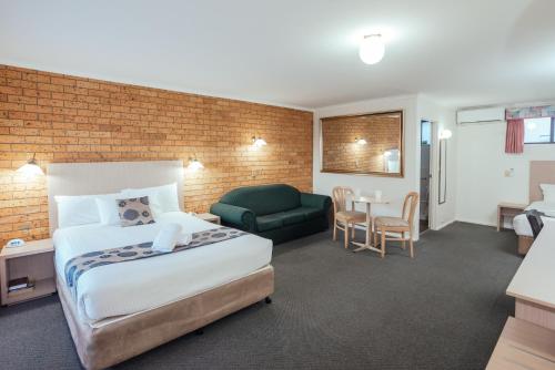 a hotel room with a bed and a couch and a chair at Coffs Windmill Motel in Coffs Harbour