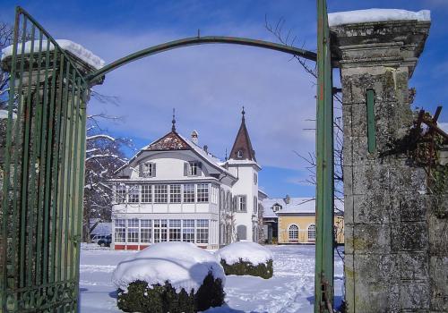 an open gate to a large white building in the snow at Château de Bossey in Bogis-Bossey