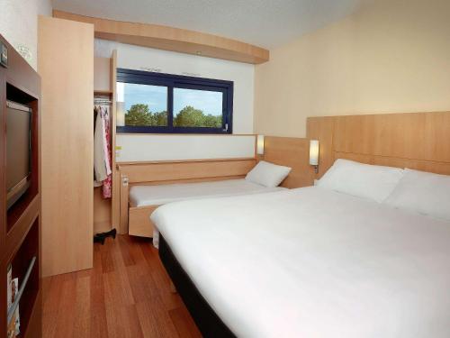 a hotel room with two beds and a television at ibis Site du Futuroscope in Chasseneuil-du-Poitou