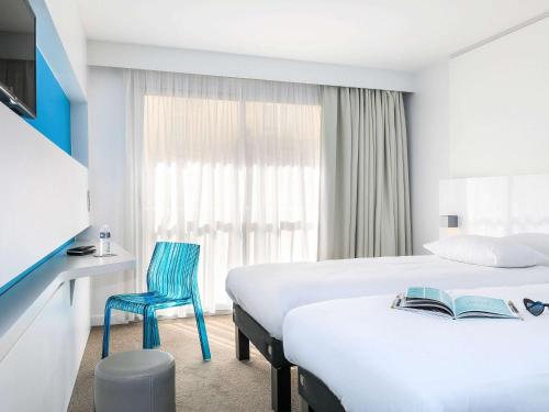 a hotel room with two beds and a blue chair at Ibis Styles Menton Centre in Menton