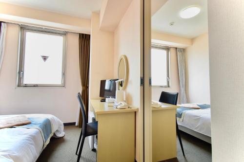 ein Hotelzimmer mit 2 Betten, einem Schreibtisch und einem Spiegel in der Unterkunft Hotel Frontier Iwaki in Iwaki