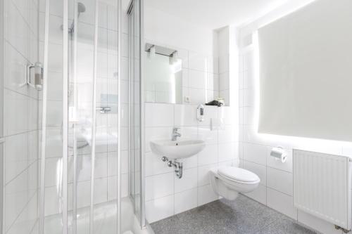 a white bathroom with a toilet and a sink at Hotel und Restaurant Zeus in Wolfsburg