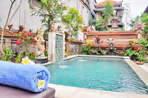 a swimming pool in a garden with a fountain at Nick's Homestay in Ubud