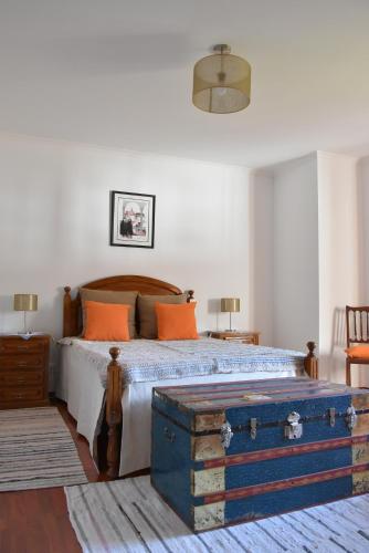 a bedroom with a bed with orange pillows and a trunk at Casa Mouramortina in Vila Nova de Poiares