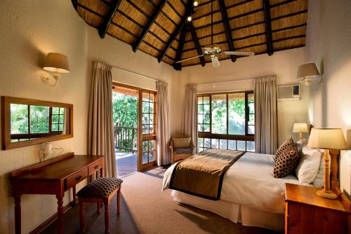 a bedroom with a bed and a desk and windows at Kruger Park Lodge in Hazyview
