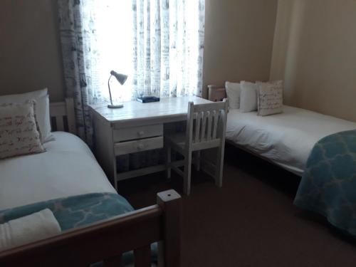 a bedroom with two beds and a desk with a lamp at Augrabies De Oude Stoor Guesthouse in Augrabies