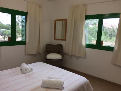 a bedroom with a bed and a chair and windows at Es Magraner in Cala Saona