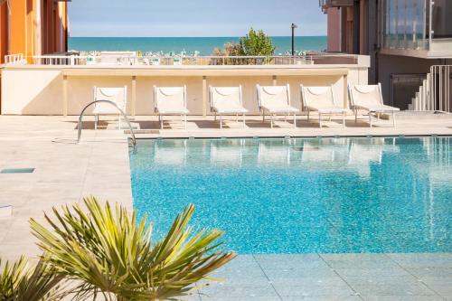 a swimming pool with chairs and the ocean in the background at Hotel Villa Maria in Caorle