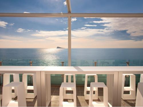 a view of the ocean from a balcony with white stools at Hotel Villa del Mar in Benidorm