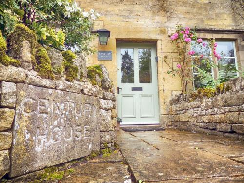 a stone house with a white door and a stone wall at Century House in Moreton in Marsh