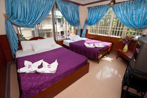 two beds in a room with blue curtains and shoes on them at Okay Guesthouse Phnom Penh in Phnom Penh