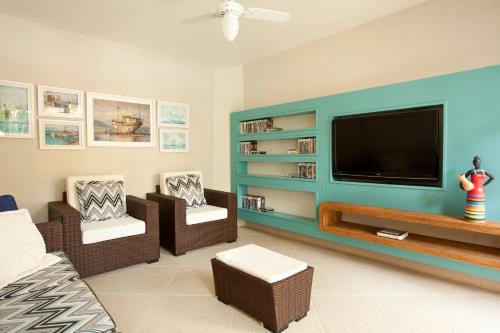 a living room with a flat screen tv and two chairs at Pousada Camburioca in Camburi