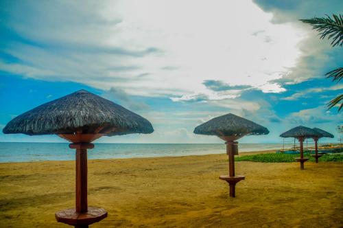 three straw umbrellas on a beach with the ocean at Camaya-an Paradise Beach Resort in Malabugas