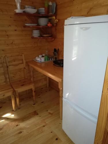 a kitchen with a white refrigerator and a wooden table at Kempings Mežmalas in Usma