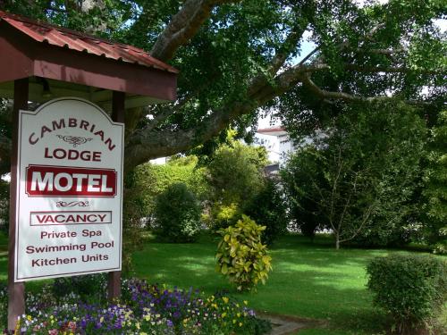a sign for a motel in a yard with flowers at Cambrian Lodge Motel in Cambridge