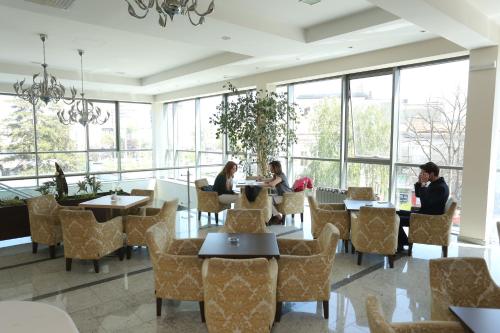 people sitting at tables in a restaurant with large windows at Hotel Kragujevac in Kragujevac
