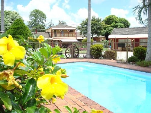 a swimming pool in front of a house with yellow flowers at Alstonville Settlers Motel in Alstonville