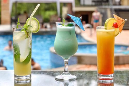 three cocktails sitting on a table next to a pool at Arhaná Hosteria & Resort in Gualaceo