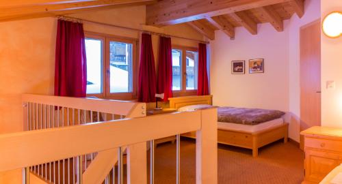 a bedroom with a bed and a staircase with red curtains at Familienhotel Garni Sporting in Bettmeralp