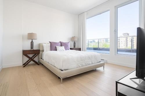 a white bedroom with a bed and a flat screen tv at Le Se7t Penthouses in Montréal