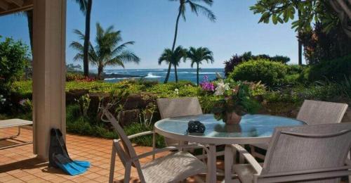 a patio with a table and chairs and the ocean at Whalers Cove in Poipu in Koloa
