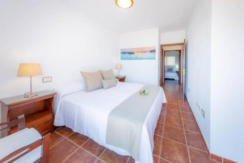 ein Schlafzimmer mit einem weißen Bett, einem Tisch und einem Stuhl in der Unterkunft Luminoso adosado frente al mar in El Médano