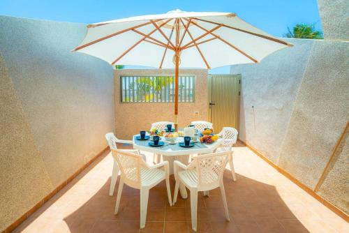 einen weißen Tisch mit Stühlen und einem Sonnenschirm in der Unterkunft Luminoso adosado frente al mar in El Médano