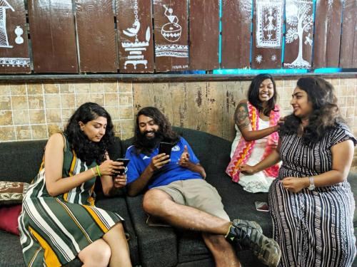 a group of people sitting on a couch looking at their cell phones at Backpackers Villa Mumbai in Mumbai