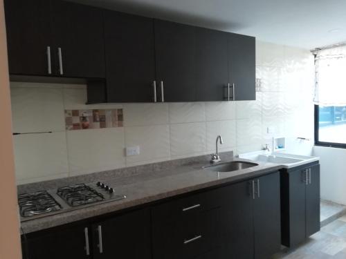a kitchen with black cabinets and a sink and a stove at Apartamentos Paipa in Paipa