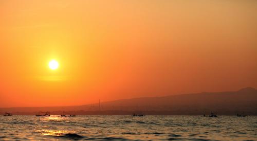 a sunset over the ocean with boats in the water at Puri Saron Hotel Baruna Beach Lovina in Lovina