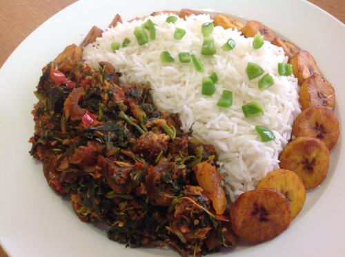 a white plate with rice and vegetables on a table at Adis Hotels Ibadan in Ibadan