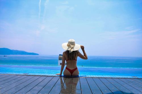 a woman in a bikini sitting next to a swimming pool at Grand Ocean Luxury Boutique - Infinity Rooftop Pool in Da Nang