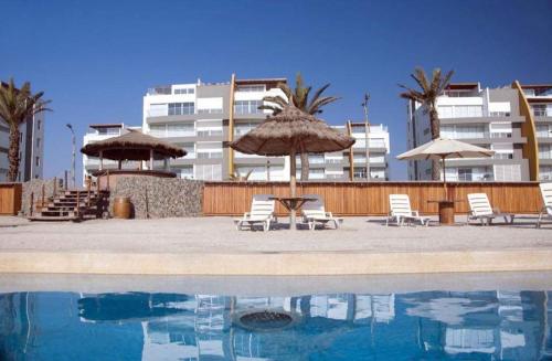 una piscina con sillas y sombrillas junto a un edificio en Apartamento con vista a Islas Ballestas, en Paracas