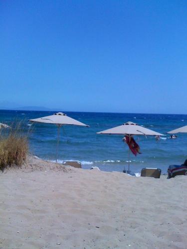 three white umbrellas on a beach with the ocean at Calypso Apartments in Artemida