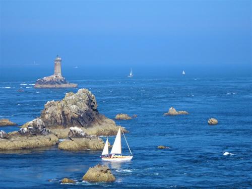 a small sail boat in the water with a lighthouse at Chambre d hôtes O beurre salé in Cléden-Cap-Sizun