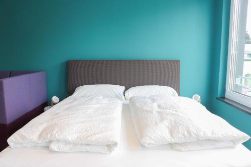 a bed with two white pillows and a blue wall at Das Fischer Boardinghouse BW in Bad Wörishofen