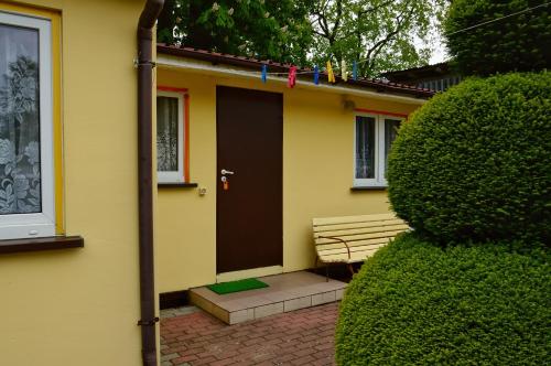 a yellow house with a brown door and a bench at Domki letniskowe U GOSI in Trzęsacz
