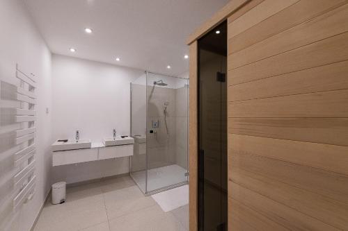 baño con ducha, 2 lavabos y puerta de cristal en OliverLux Aparthotel, en Tihany