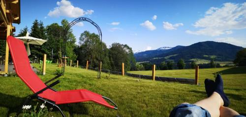 a person laying on the grass next to a red chair at Landhaus Desiree in Hopfgarten im Brixental