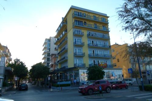 un grand bâtiment jaune avec des voitures garées devant lui dans l'établissement Hotel Ideal Sottomarina, à Sottomarina