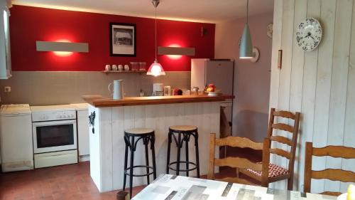 une cuisine avec des murs rouges, un comptoir et des tabourets dans l'établissement La roseraie de Camille, à Mont-sous-Vaudrey
