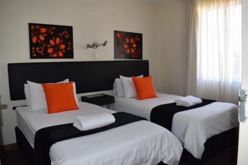 Habitación de hotel con 2 camas con almohadas de color naranja en Premiere Classe Apartment Hotel, en Johannesburgo