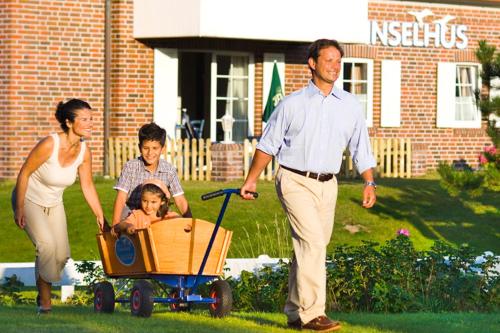 a man and a woman pushing a child in a wagon at Hotel Strandhof in Baltrum