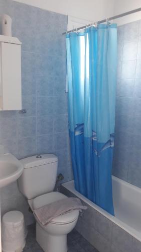 a bathroom with a toilet and a blue shower curtain at Chaniotis Studios in Kalafatis