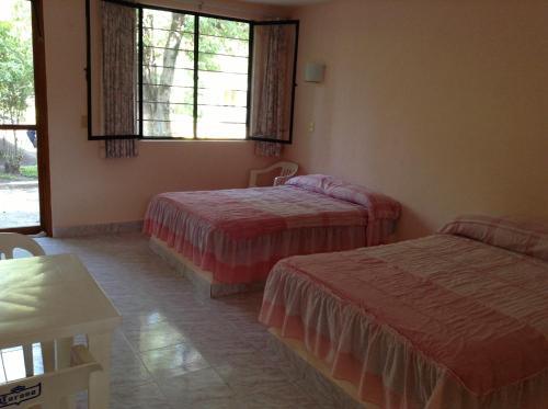 a bedroom with two beds and a window and a table at Hotel Tecozautla in Tecozautla