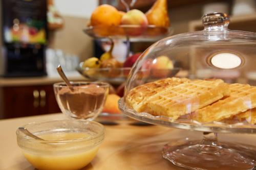 a glass plate with waffles on a table with a bowl of fruit at Gold House Pension in Balatonfüred
