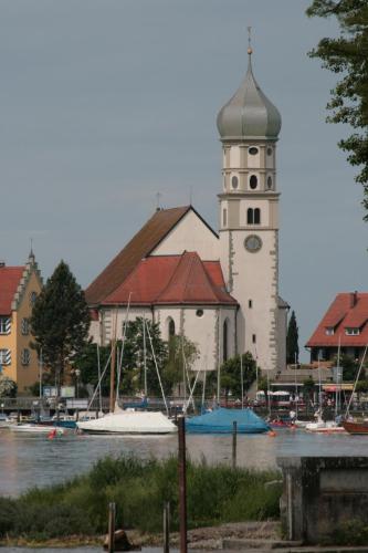 a church with a clock tower next to a body of water at Hotel-Restaurant Walserhof in Wasserburg am Bodensee