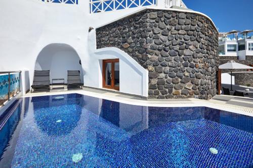 a swimming pool in a villa with a stone wall at Petit Palace Suites in Fira