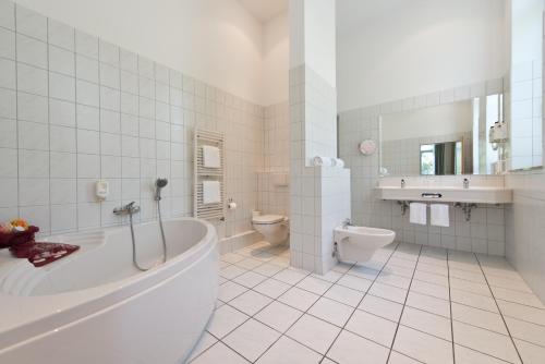 a bathroom with a tub and a toilet and a sink at Hotel Bollmannsruh am Beetzsee in Päwesin