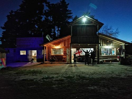 two people standing outside of a log cabin at night at Heshkili huts and cabins Svaneti in Keshkili
